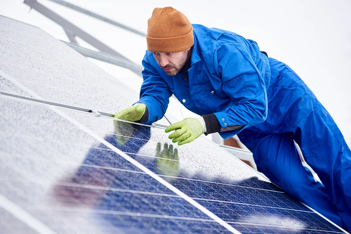 Worker in blue coveralls and brown beanie inspecting solar panels, emphasizing solar panel services and expertise in solar detach and reset projects.