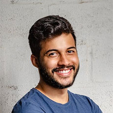 Smiling man with short dark hair and beard, wearing a blue shirt, standing against a textured wall, representing professionalism and customer satisfaction in solar energy solutions.