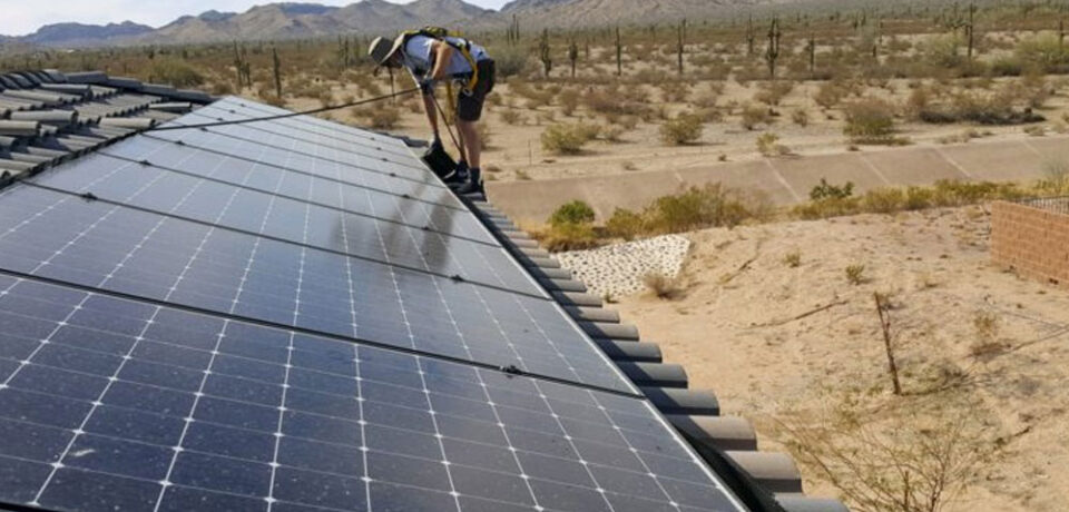 Worker performing solar panel detach and reset service on a roof in Arizona, surrounded by desert landscape and cacti.